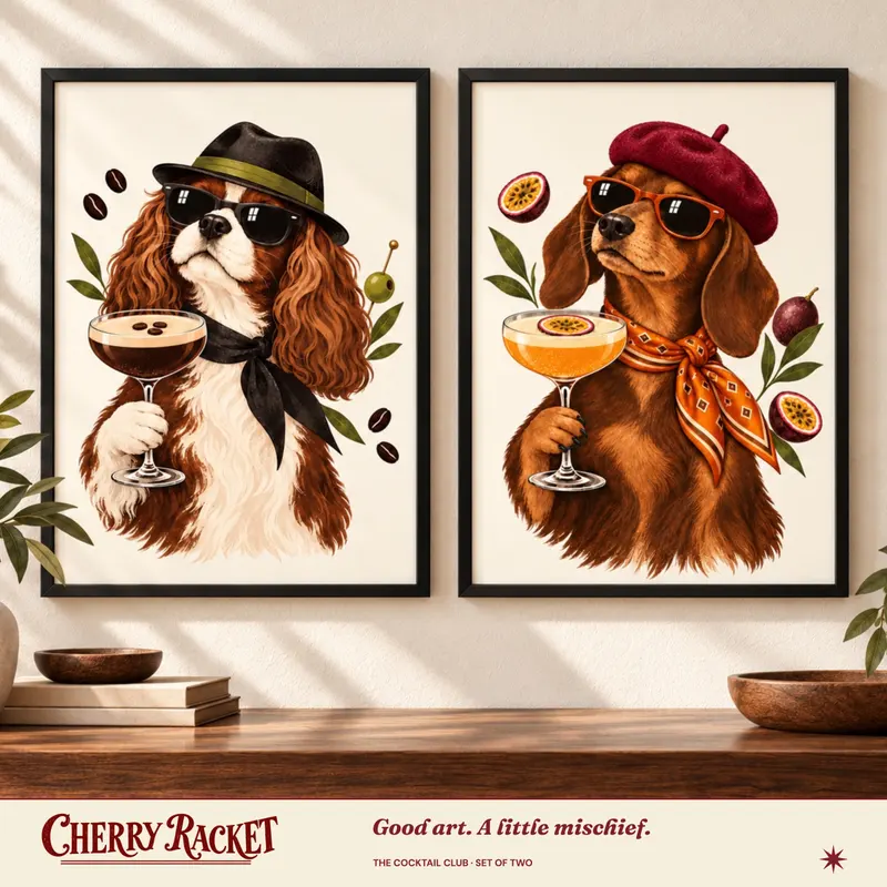 Styled room mockup showing the Cavalier Espresso Martini and Dachshund Pornstar Martini prints together. Frames not included.